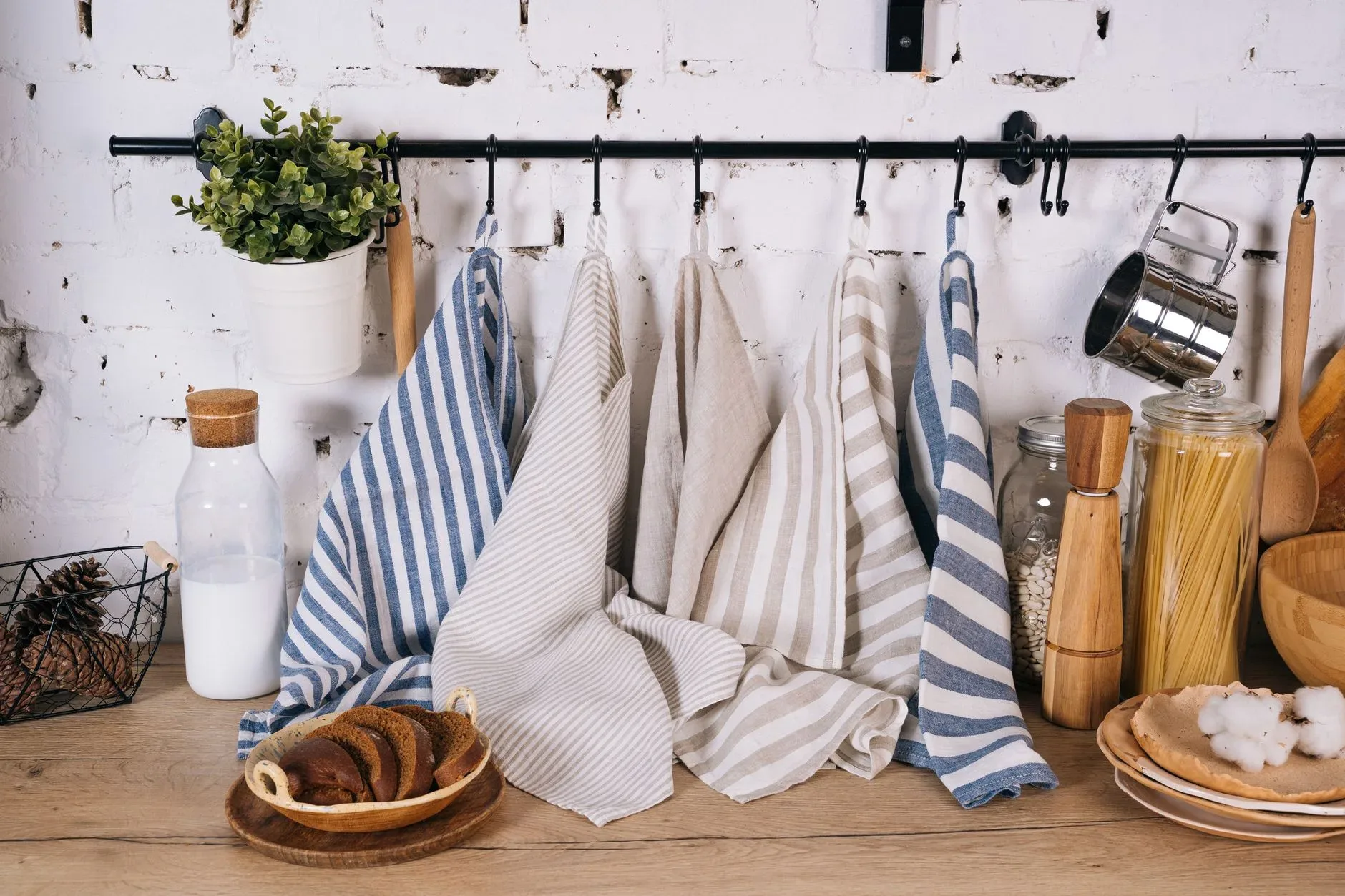 A cozy kitchen scene featuring striped towels, jars of pasta, milk bottle, and rustic decor on a wooden table.