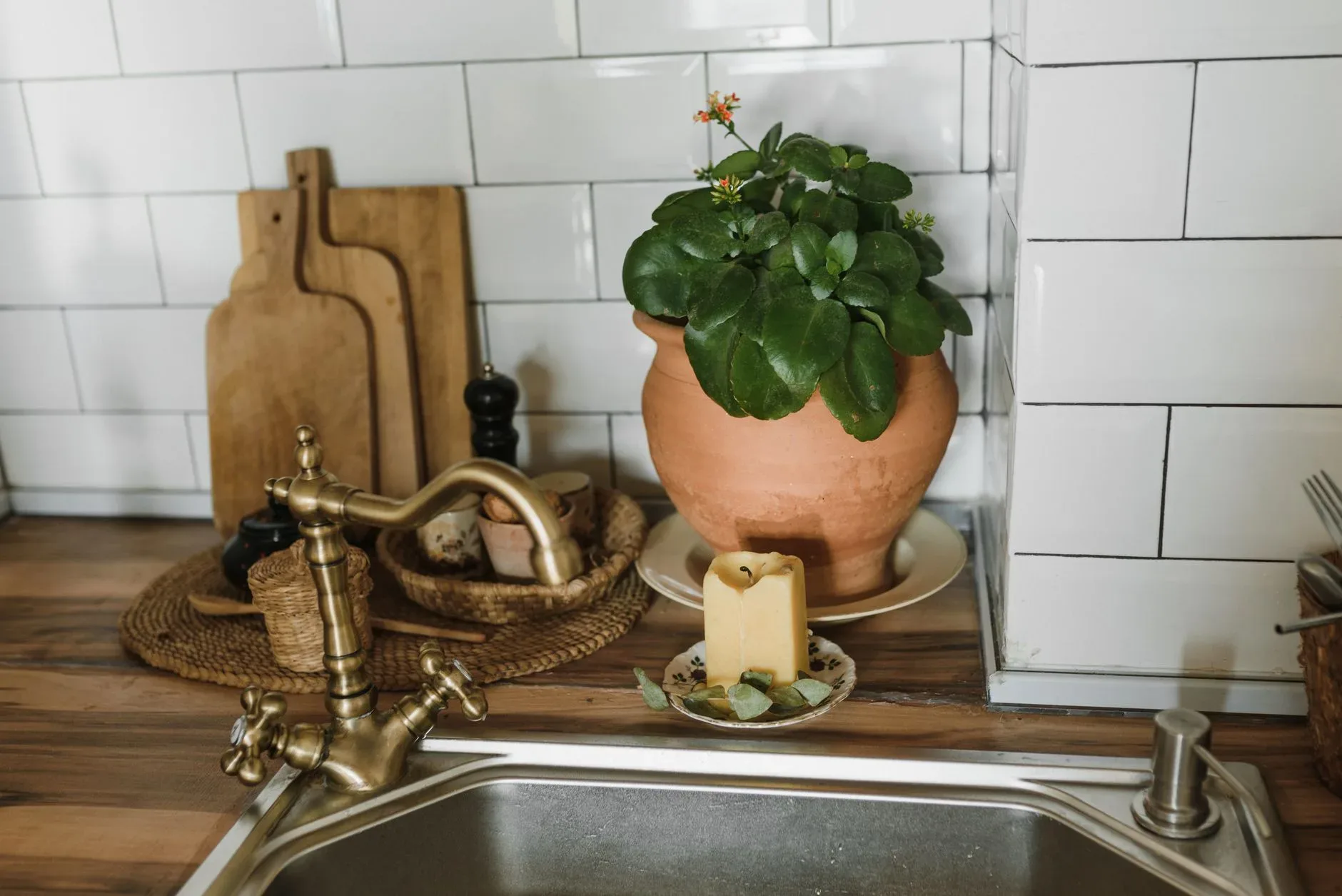 A cozy kitchen setup featuring a terracotta pot, green plant, and a lit candle next to a faucet.