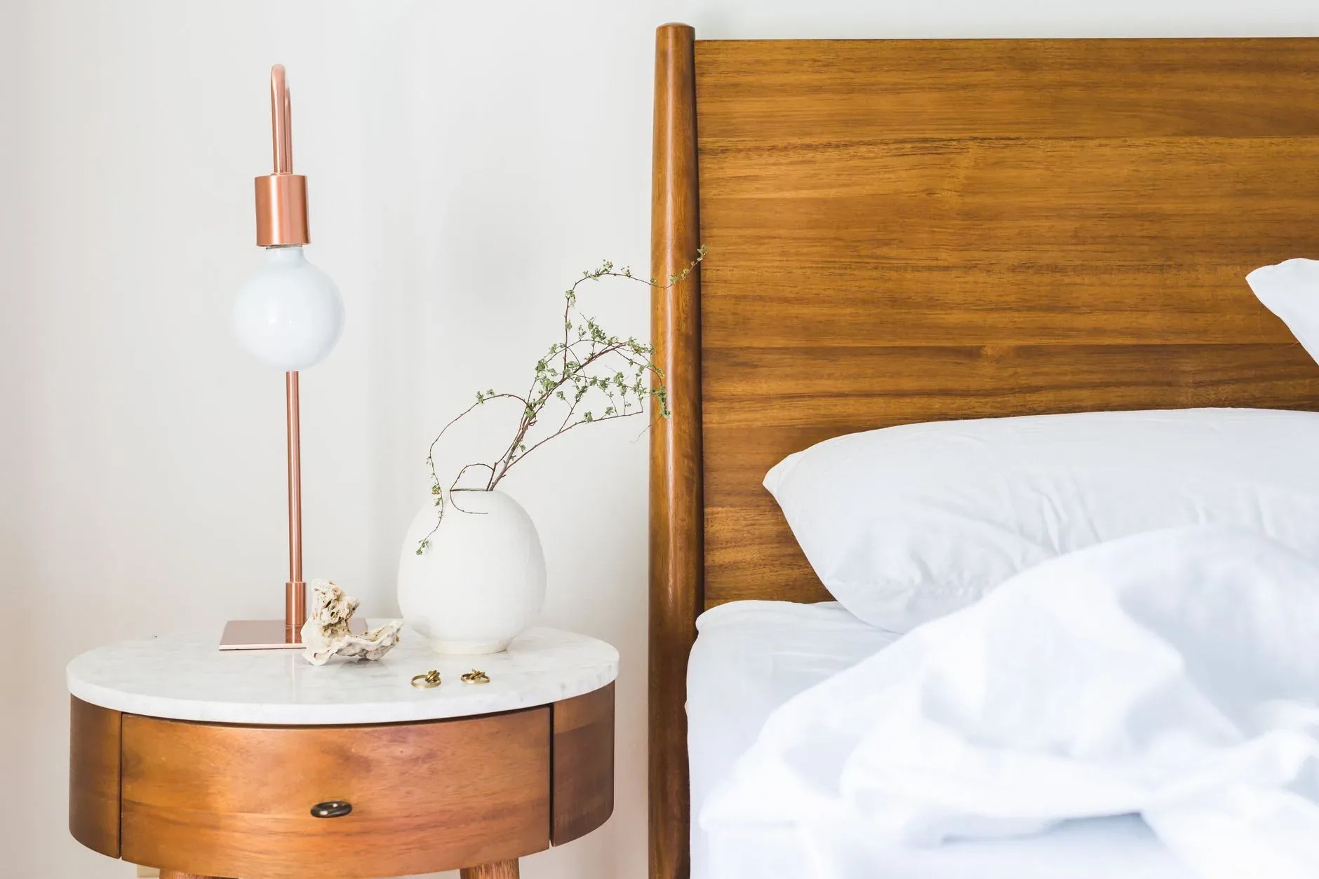 A modern bedroom setup featuring a wooden bed, stylish lamp, and round side table with a plant.