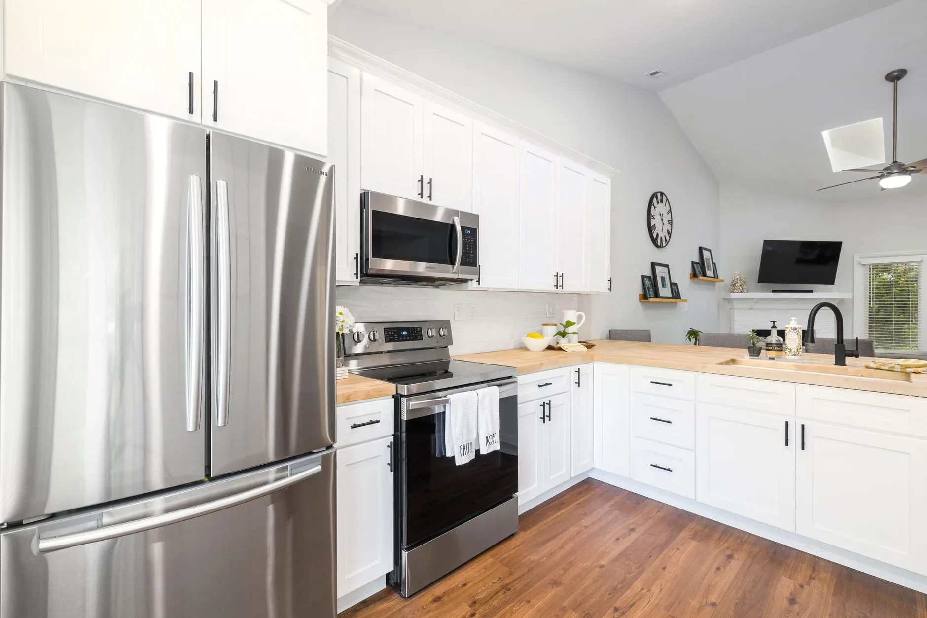 Bright modern kitchen featuring white cabinets, wood countertops, and stainless steel appliances.