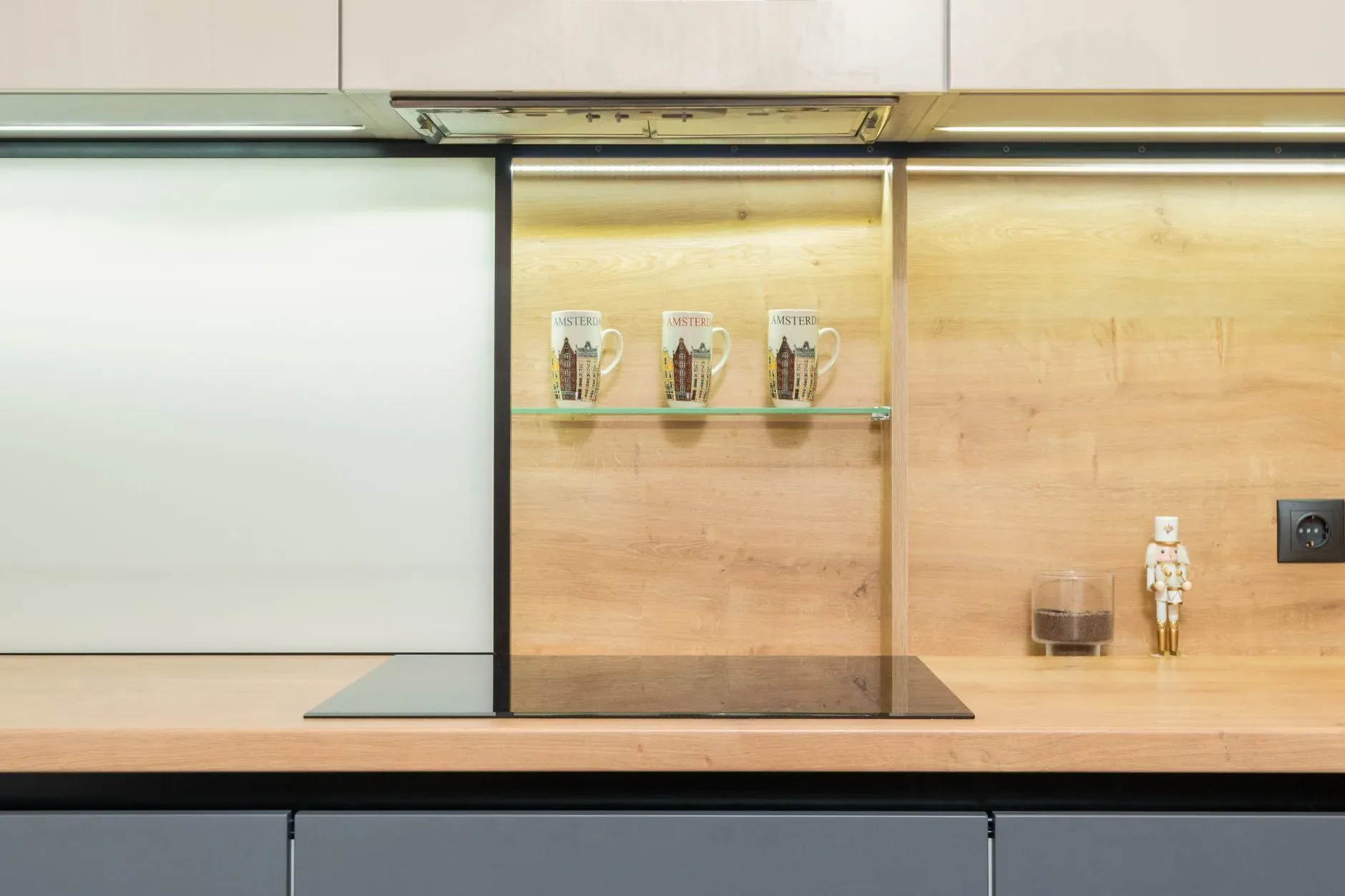Built in stove under hood and shelf with mugs against statuette on wooden table in modern kitchen at home