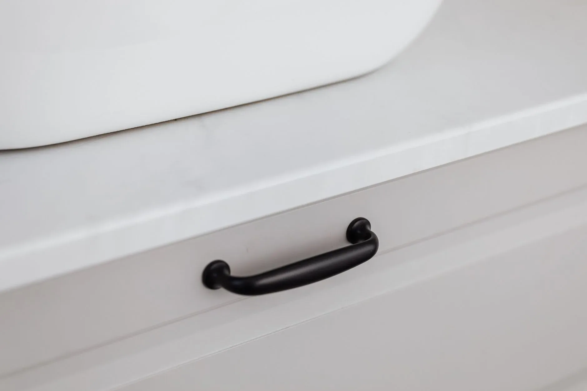 Close-up of a modern black handle on a white drawer, showcasing minimalist interior design.