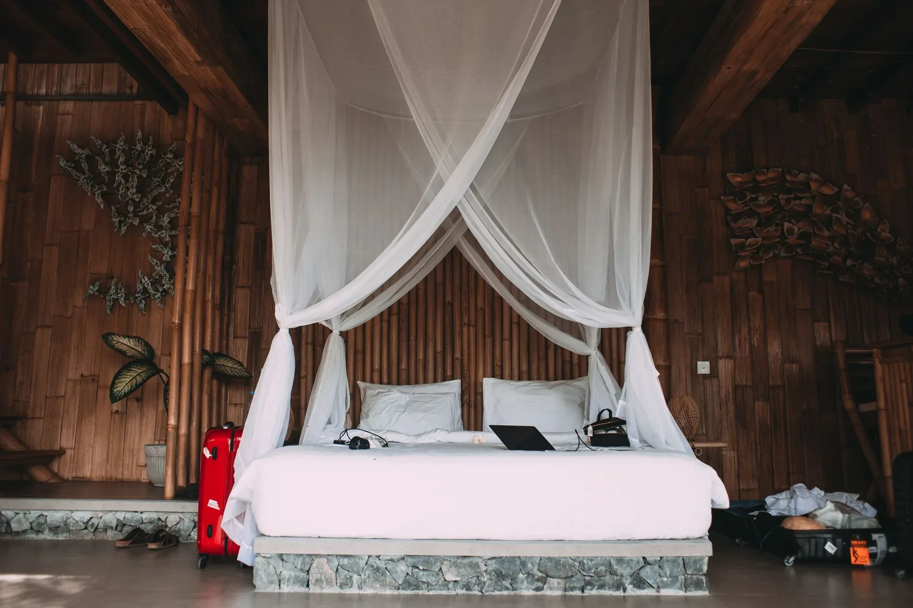 Comfortable bed with netbook and headphones near suitcases and bamboo walls in hotel room