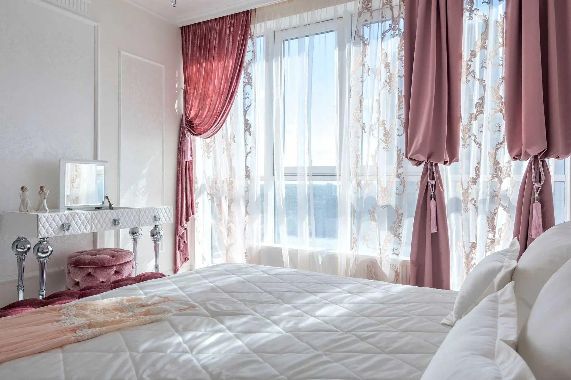 Cozy and elegant white and rosy bedroom with comfortable bed and draped curtains