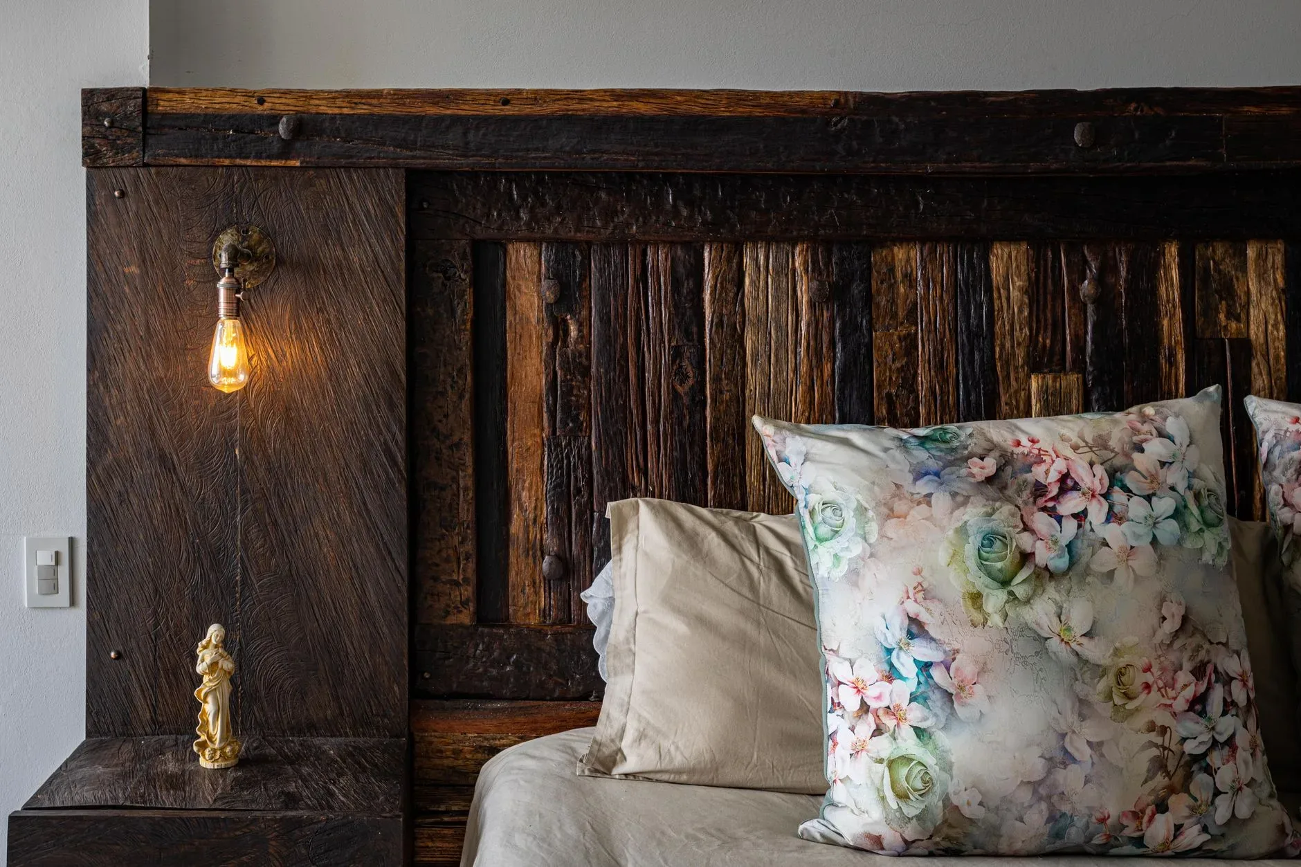 Cozy bedroom corner featuring a rustic wooden headboard and floral pillows in ChÃa, Colombia.