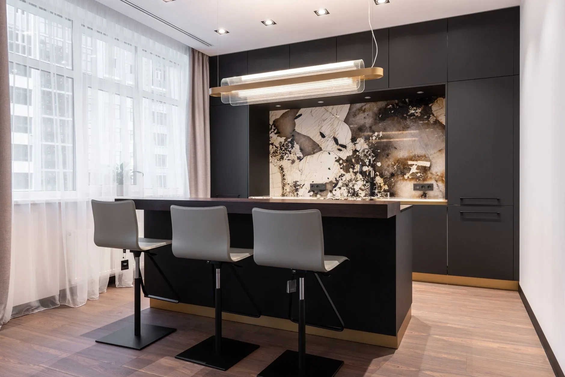 Interior of contemporary kitchen with marble panel over cooking zone and bar counter with chairs