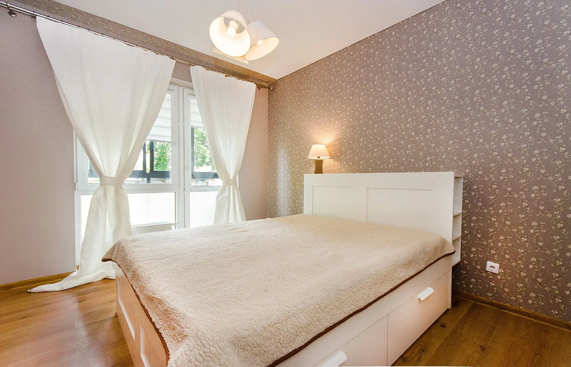 Inviting bedroom with neutral tones, cozy bedding, and ample natural light streaming through curtains.