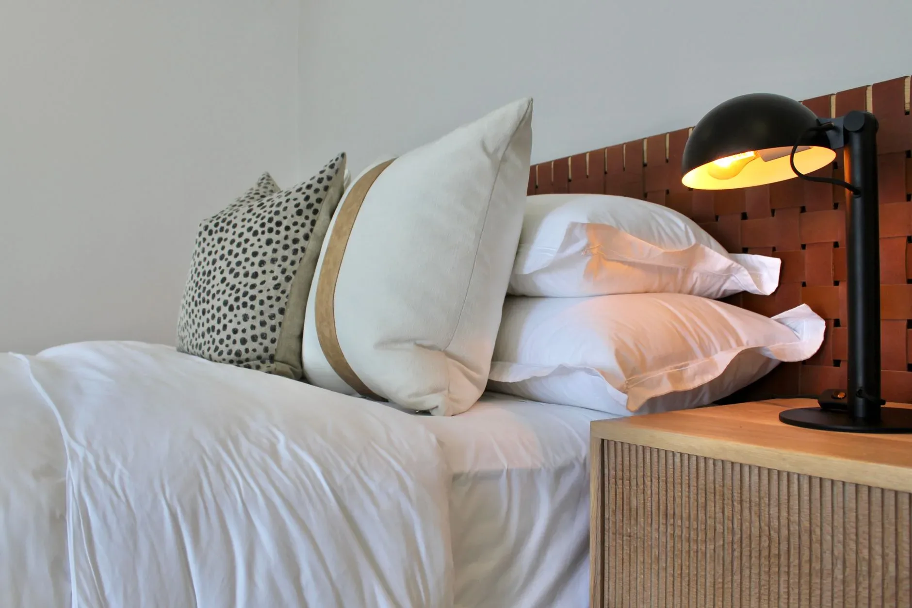 Modern bedroom interior featuring white bedding, patterned cushions, and a stylish black lamp.