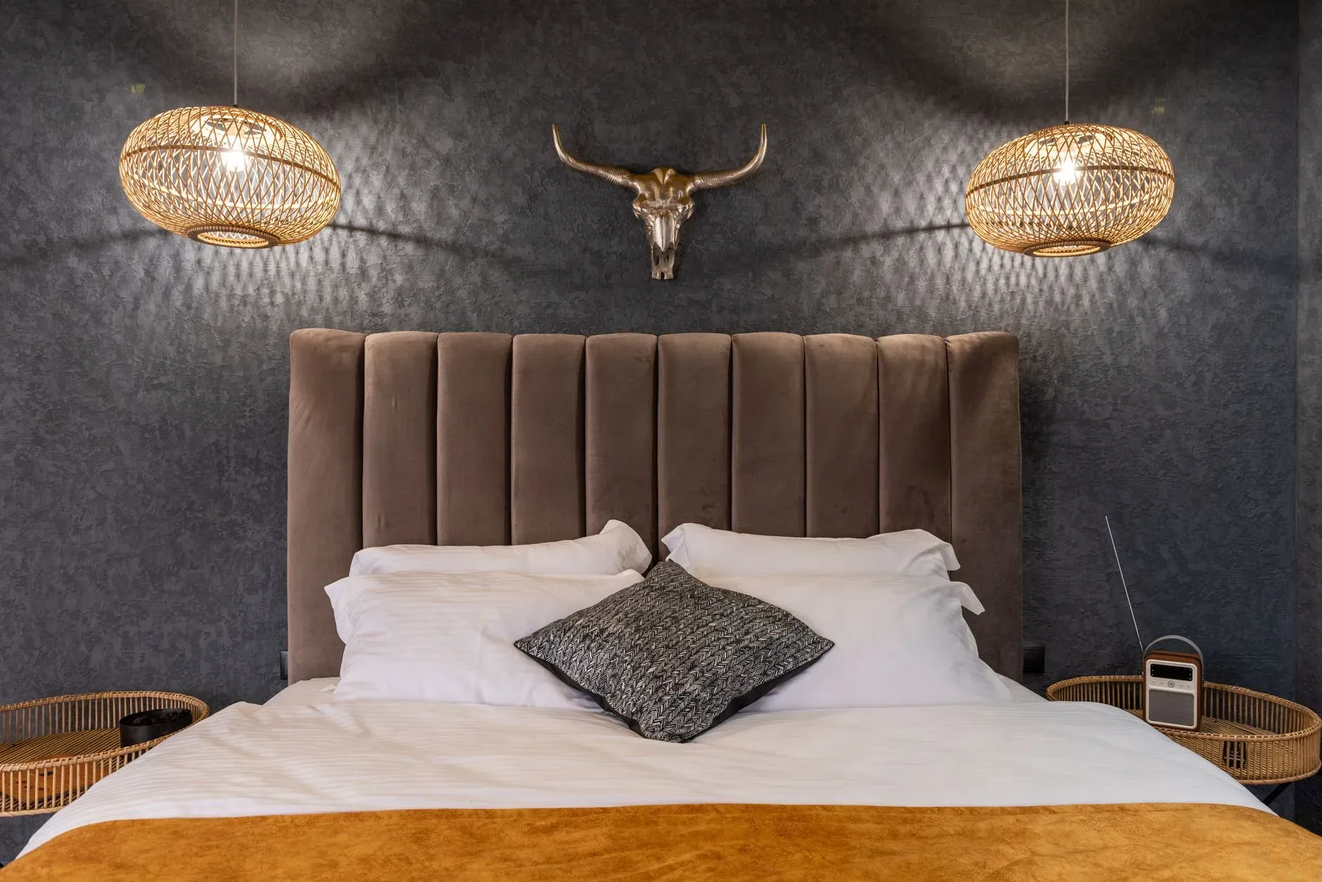 Modern bedroom interior with cushions on soft bed between glowing lights and wicker trays with radio in hotel