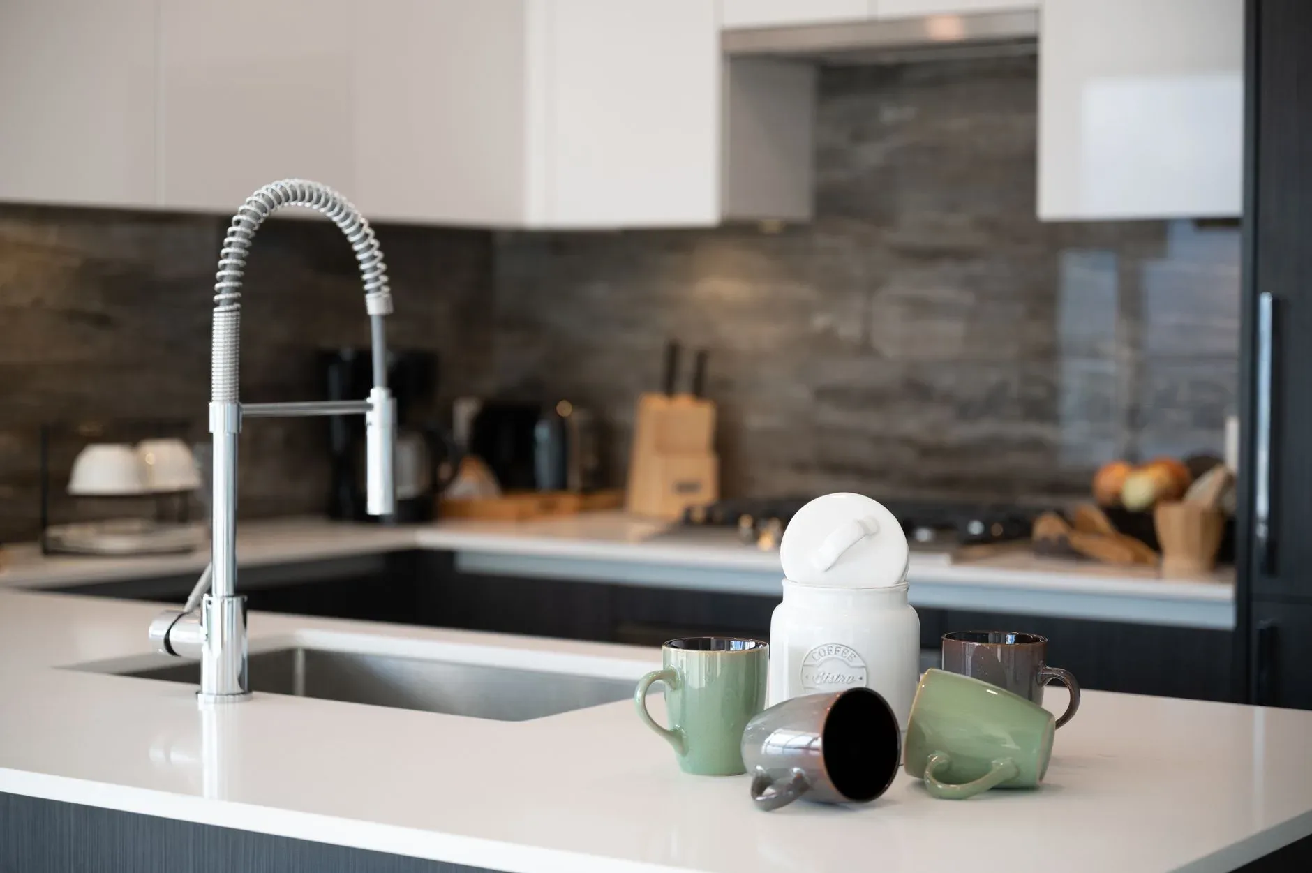 Sleek kitchen design featuring a coffee canister and mugs on a white countertop.