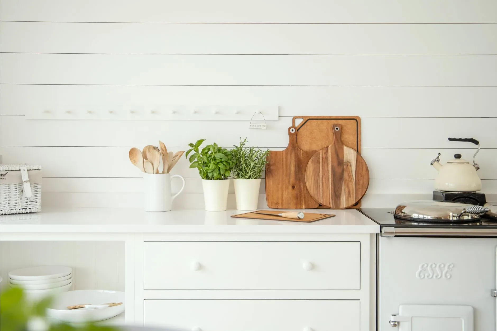 Stylish kitchen counter with herb pots, cutting boards, and utensils against a white backdrop.