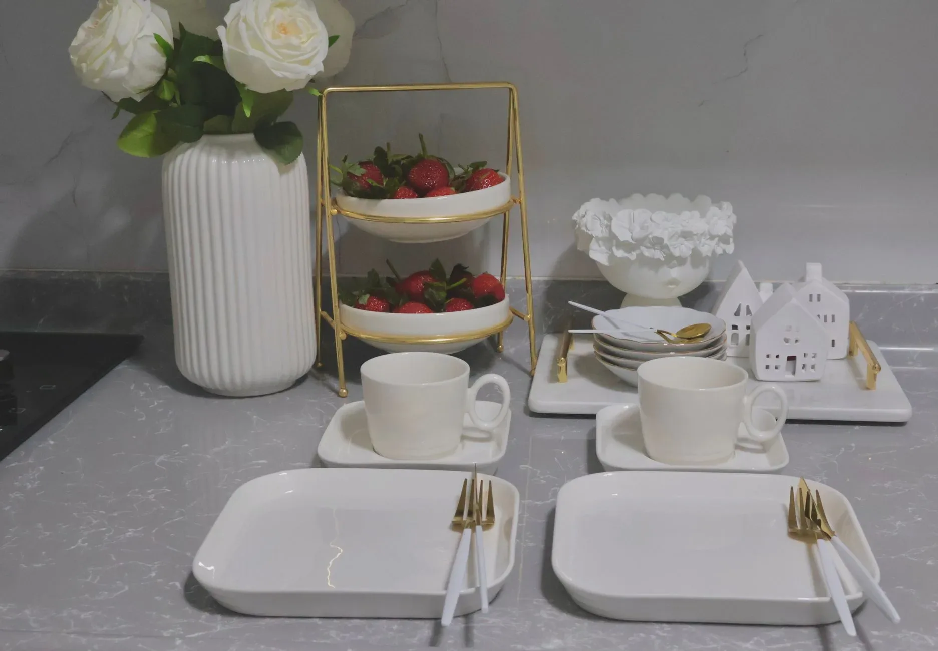 Stylish table setup with white dinnerware, roses, and strawberries in a modern kitchen.