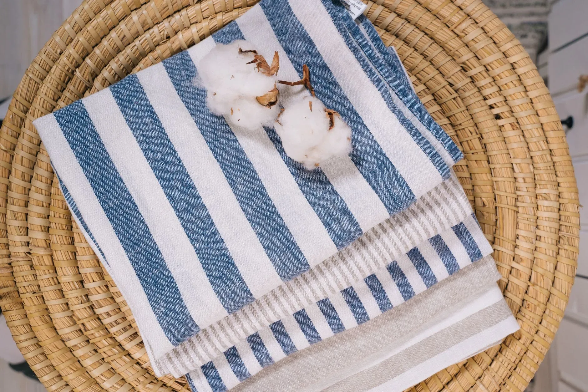Top view of striped linen towels with cotton flowers on a rattan surface.